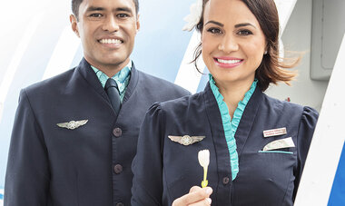 Hotesse air tahiti nui qui tend une fleur de tiare au passager
